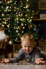 Fototapeta na wymiar А little cute boy writes a letter to Santa Claus, dresses up a Christmas tree and dreams of a miracle on the background of the Christmas interior.