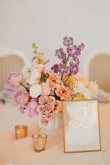 Coziness and style. Modern event design. Table setting at wedding reception. Floral compositions with beautiful flowers and greenery, candles, laying and plates on decorated table.