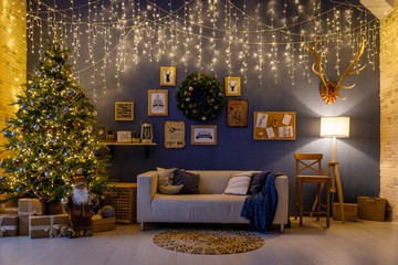 Christmas and New Year interior - blur background: fireplace, lamps, green Christmas tree, brown leather sofa, gifts, candles, moose rocking chair. Lots of lights glowing in the dark.