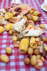 Fototapeta na wymiar Crab claw in a seafood boil with corn and potatoes, on a red checkered table cloth