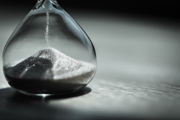 Sand running through the bulbs of an hourglass measuring the passing time in a countdown to a deadline, on a bright background with copy space.