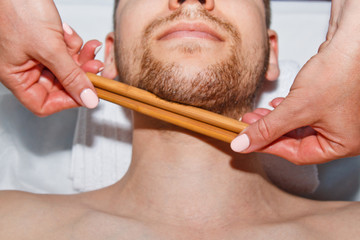 Wellness concept. Professional masseur gives a man a Thai facial massage with special sticks in a spa center. Relaxation and recovery after work.