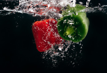 Red and green peppers in water on a black background.