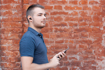 Modern man listening music by bluetooth earphones. Guy control wireless headphones from his...