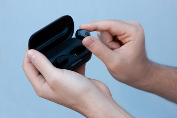 Black wireless headphones in the hands of a white man on a gray background. Bluetooth headphones in a case.