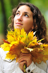 Naklejka premium Closeup portrait of a dreamy beautiful young curly girl looking up and holding a bouquet of yellow maple leaves in her hands. The concept of the onset of autumn and student time