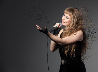 Beautiful young girl singer sings into a microphone in a beautiful black dress with notes around on a gray background. Concept of art.
