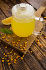 Hot sea buckthorn tea in the glass teapot on the brown  wooden background. Healthy medical drink. Location vertical.