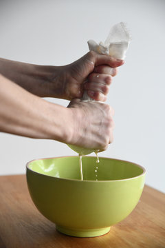 Hands wringing out a cheesecloth into a green bowl