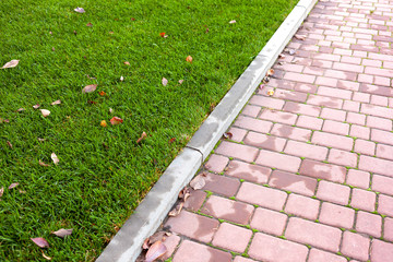 Styling paving slabs. Red paving slab next to a luxurious green lawn.