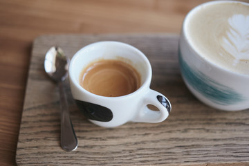A cup of espresso with a cup of cappuccino standing on a wooden table in a cafe.