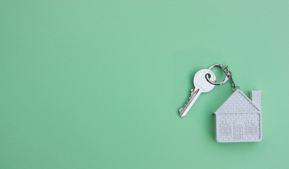 White key with a keychain in the form of a house on a light green background. The concept of buying, selling, renting real estate, mortgages, your own home. Place for text