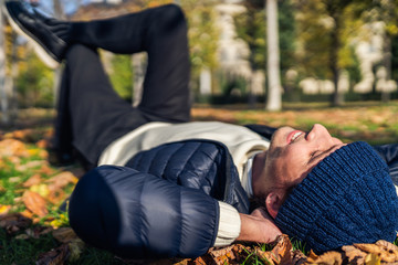 Happy young man relaxing in the park among autumn leaves.