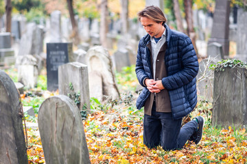 Mourning young man kneeling in front of a grave on a cemetery