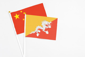 Bhutan and China stick flags on white background. High quality fabric, miniature national flag. Peaceful global concept.White floor for copy space.