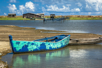Fototapeta na wymiar Pond with boat, fishing nets and wooden house in the background.