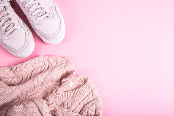 Women fashion clothes on pastel pink background. Sweater, sneakers. Flat lay, top view
