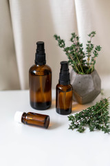 Essential oils in glass bottles and fresh thyme herb on white drapery background. Aromatherapy concept photo, vertical orientation.