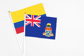 Fototapeta premium Cayman Islands and Colombia stick flags on white background. High quality fabric, miniature national flag. Peaceful global concept.White floor for copy space.