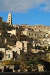 Obraz premium Panorama of the Sassi of Matera with houses in tuff stone. Church and bell tower at dawn with sky and clouds.