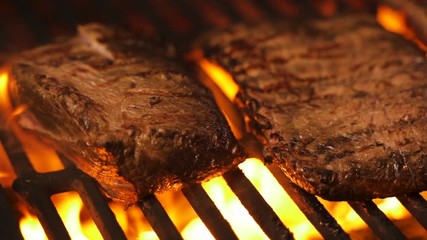 A few delicious pork or beef steaks are grilled over a live fire. Classic foods preparation. Pork steak on flaming grill barbecue. Gourmet cooking roasted meat. Cook in picnic. Organic food processing