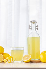 A glass of lemon juice and lemons around on a table.