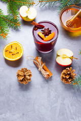 Mulled wine with spices in glass. Red mulled wine with cinnamon, anise and honey. Hot mulled wine at a cement gray background with fir branches and pine cones
