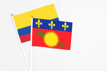 Guadeloupe and Colombia stick flags on white background. High quality fabric, miniature national flag. Peaceful global concept.White floor for copy space.