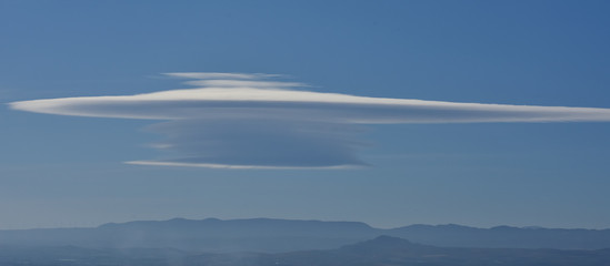 Huge lenticular cloud in an intense blue sky over the distant mountains