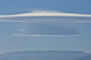 Huge lenticular cloud in an intense blue sky over the distant mountains
