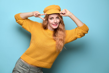 Easy-going Woman happy smiling in Stylish fashion yellow colored outfit. Beautiful young Girl in Trendy jumper, make up. Joyful lady shows peace sign in yellow cap, fashionable happiness concept
