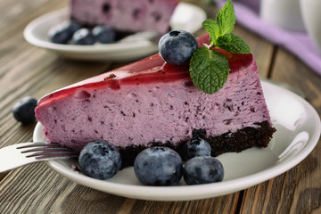 Slices of blueberry mousse cake with mirror glaze decorated berries and leaves of mint are on wooden table, close up