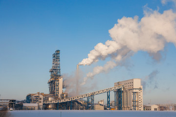 Oil refinery in sunny winter day with smoke from pipes in blue sky