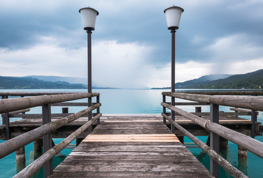 Steg am Attersee mit zwei Laternen, im Hintergrund sieht man Berge und den Horizont
