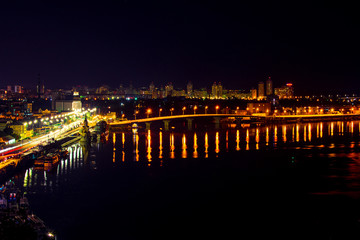 Fototapeta na wymiar Night city landscape. Landscape of the city of Kiev in the night. A bridge across the river with bright colored lights. Night view of the capital of Ukraine
