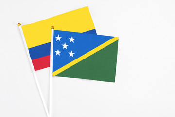 Solomon Islands and Colombia stick flags on white background. High quality fabric, miniature national flag. Peaceful global concept.White floor for copy space.