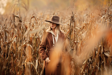 Style woman in coat and hat on corn field in autumn time season