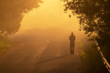An elderly man walks on the road in the morning