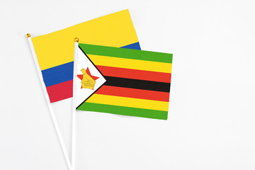 Zimbabwe and Colombia stick flags on white background. High quality fabric, miniature national flag. Peaceful global concept.White floor for copy space.