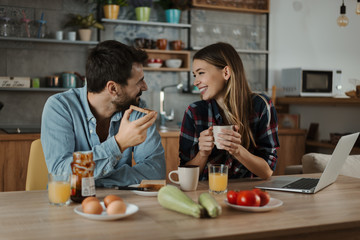  Young smiling couple communicating during breakfast time in the kitchen