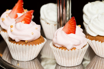 Miniature muffins decorated with cream and strawberries on the steel racks of the buffet.