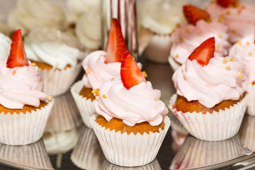 Miniature muffins decorated with cream and strawberries on the steel racks of the buffet.