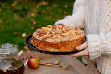 female holding apple pie, and tea on tray on table in a garden