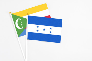 Honduras and Comoros stick flags on white background. High quality fabric, miniature national flag. Peaceful global concept.White floor for copy space.