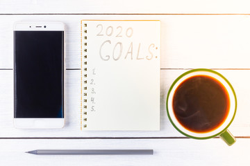 2020 new year goals, plan, action text on notepad on white wooden boards. 2020 goals on blank note paper with copy space for text and smartphone. Cup of coffee over wooden boards