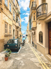 Naklejka premium Traditional Maltese street in Valetta, Malta. Narrow street with car, sky, sea and marina view. Travel and tourism in Malta concept. Cityscape of Valletta. Architecture of Valetta.
