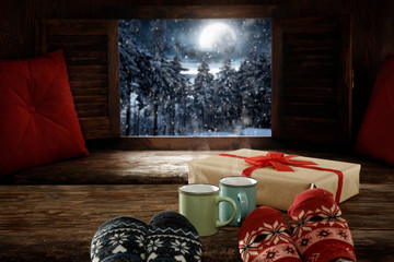 Wooden winter background of free space.Christmas december time.Woman legs with woolen socks and night landscape of forest with mountains and big moon on sky.Retro old frame and pillows decoration.