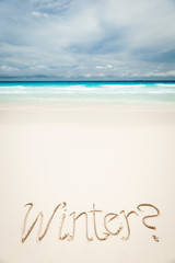 Cheeky Winter message handwritten on bright tropical beach lapped by turquoise waters