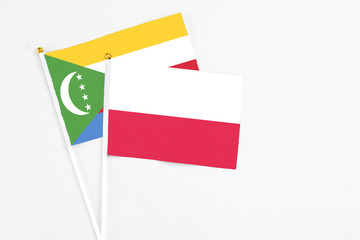 Poland and Comoros stick flags on white background. High quality fabric, miniature national flag. Peaceful global concept.White floor for copy space.