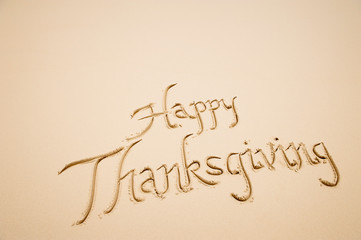 Happy Thanksgiving message handwritten in simple calligraphy script on smooth sand beach 